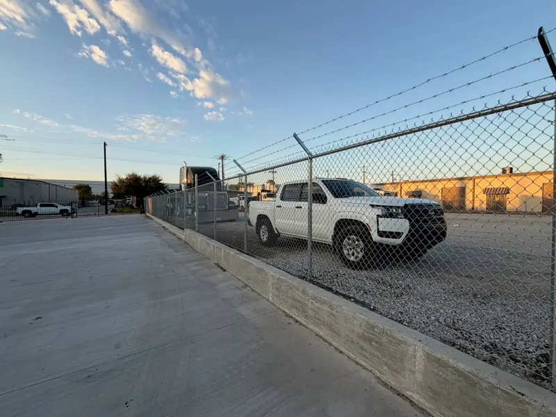 Commercial chain link fence with barbed wire on a concrete curb in Fort Worth